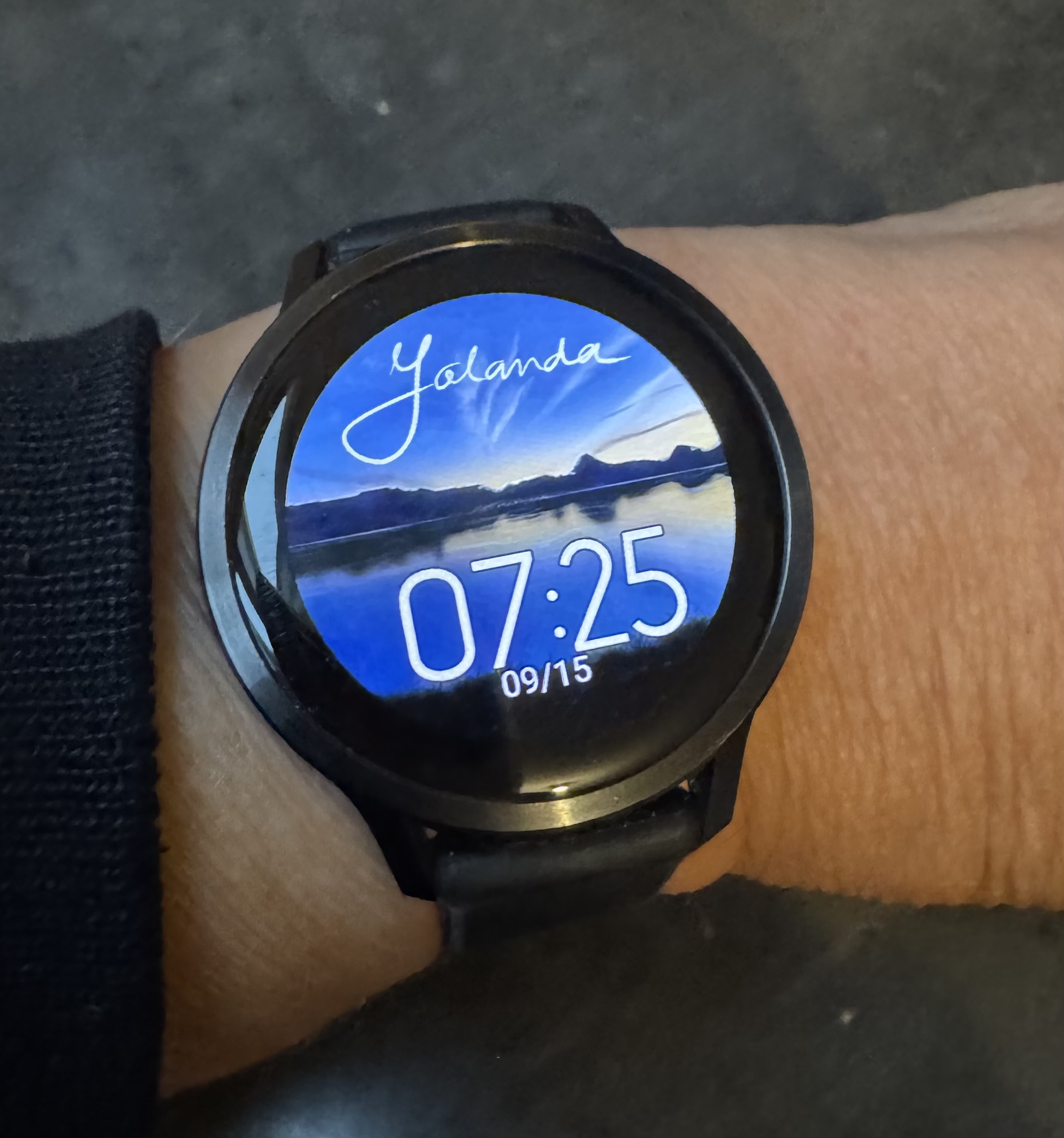 Horloge met de blauwe bergentekening als wijzerplaat en de naam Jolanda bovenaan.